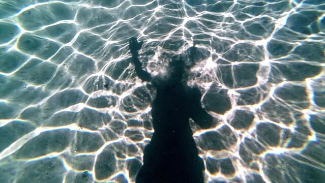 Artistic underwater shot of a swimming person's silhouette on the ocean floor.