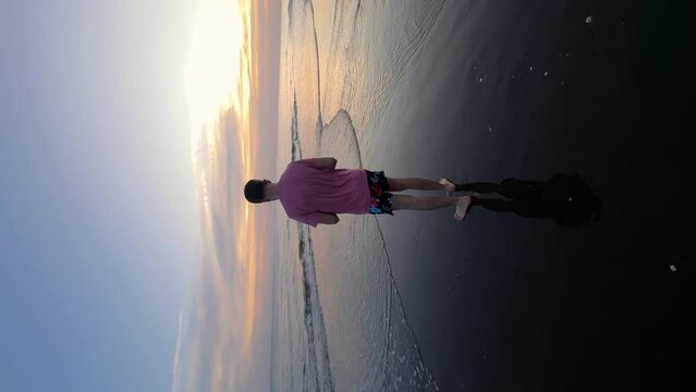 Vertical shot of Young man taking pictures of the sea with his mobile phone at sunset.