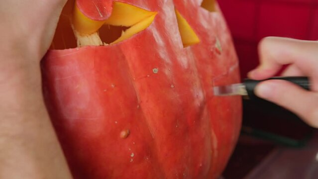 Knife carving a creepy smile on big pumpking for Halloween decoration, spooky Jack-o-lantern decor close-up
