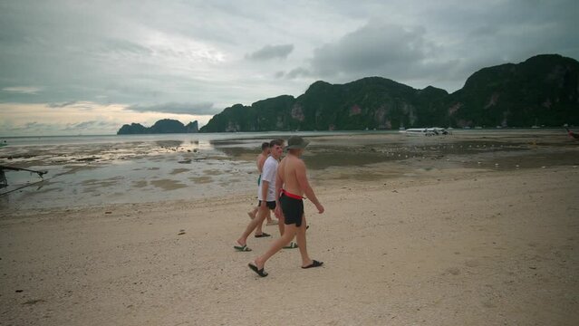 Footage of 4 model man walking on a beach in PhiPhi islands in Thailand. with incredible landscapes and nature all around. Ocean, sea, hills, jungle, forest, and local Thai boats in the background