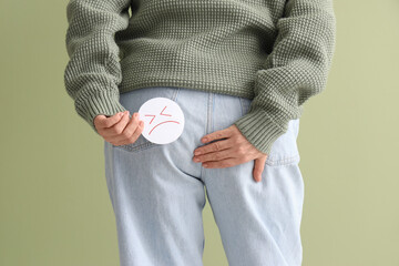 Mature woman with sad smile on green background, back view. Hemorrhoids concept
