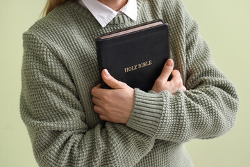 Mature woman with Holy Bible praying on green background, closeup