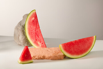 Two blocks of stone arranged over gray background with some slices of watermelon. The benefits of watermelon for the skin go way beyond just hydration. Product presentation on the stone
