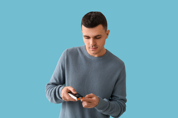 Diabetic young man using glucometer on blue background