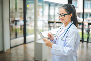 Portrait doctor with a stethoscope and using digital tablet stands confidently ready for healthcare visitor in hospital or clinic.
