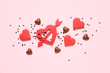Obraz na płótnie Canvas Tasty cookies, chocolate candies and red heart with arrow on pink background. Valentine's Day celebration