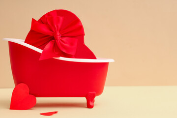 Mini bathtub with gift box and paper hearts on beige background. Valentine's Day celebration