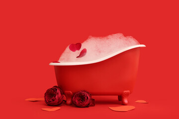 Mini bathtub with soap foam, roses and paper hearts on red background. Valentine's Day celebration