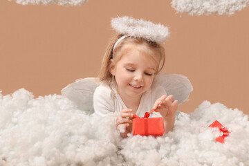 Cute little girl dressed as cupid with gift boxes and clouds lying on brown background. Valentine's...
