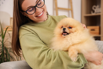 Young woman with cute Pomeranian dog resting on sofa at home, closeup