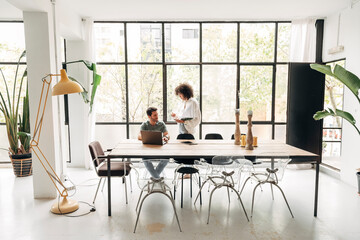 Young multiracial people interacting in spacious bright co working office with big window, - obrazy, fototapety, plakaty