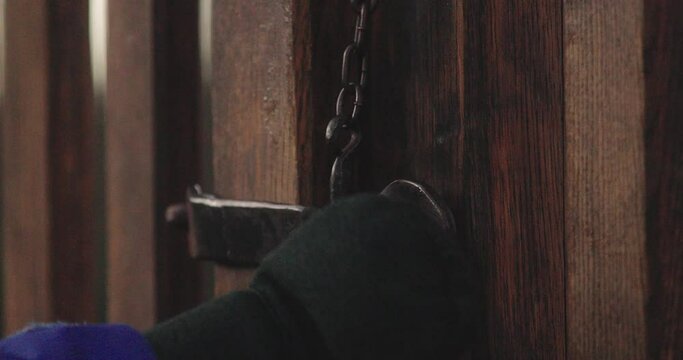 Close-up of a hand pulling an old latch out of the lock of an old wooden gate