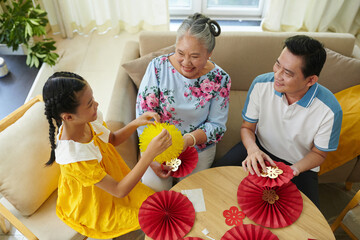 Girl enjoying making paper decorations for Lunar New Year with her father and grandmother