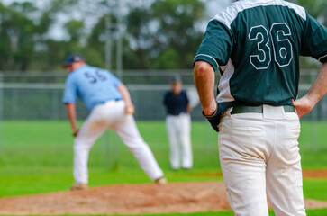 Baseball game, runner on the first base is watching the pitcher and getting ready to steal the second