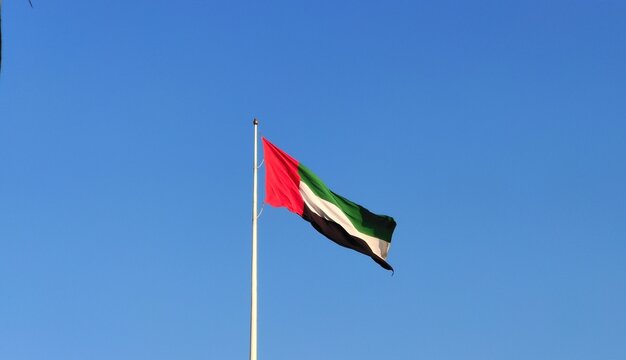 United Arab Emirates (UAE) country official national fabric or cloth flag on a flagpole flying isolated in the air by the wind on a blue sky background with copy space. Arab National Day concept.