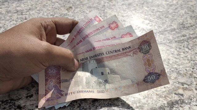 Person hand holding three hundred and fifty dirhams (AED) united arab emirates (UAE) national currency banknotes closeup macro detail view. Emirate business, money, bills, finance and cash concept.