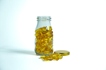 Fish Oil supplement capsules for health spill out from clear glass bottle with golden cap isolated on white background.