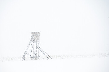 Hunting tower in countryside during snowstorm. Snowy hunting lookout in field at winter season.