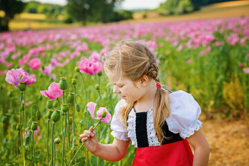 Little preschool girl in poppy field. Cute happy child in red riding hood dress play outdoor on...