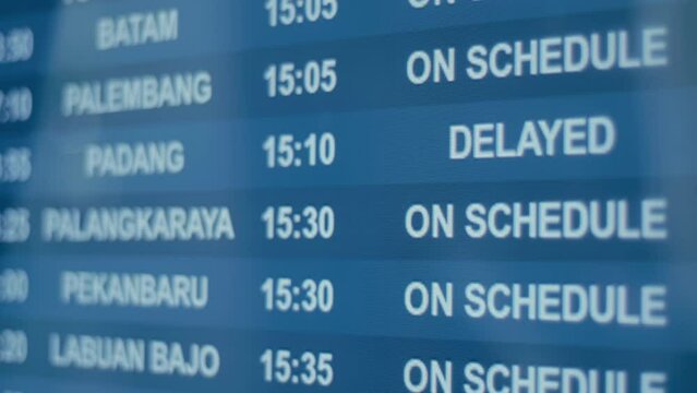 Screens of flight schedules for various cities in Indonesia show updates on the status of flight delays and arrivals at the airport while people pass by
