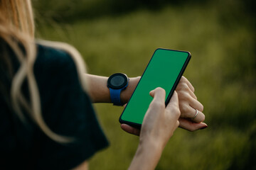 Active Caucasian woman running in nature, checking her phone and a smartwatch for fitness updates. Focus on hands