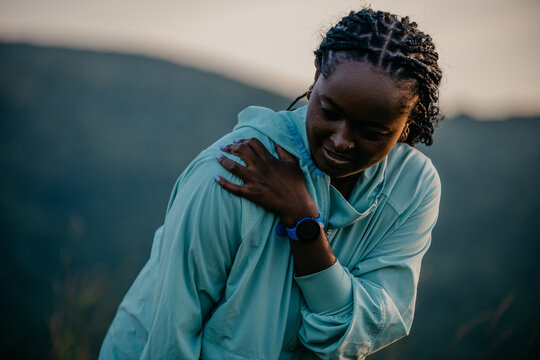 Black female runner stretching her upper body and feeling pain in the shoulder