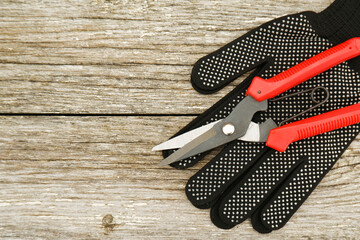 There are scissors with red pruning handles and black work gloves on a white wooden table. Garden hand pruners. Garden shears. Sharp trimmers for pruning trees and shrubs.Copyspace