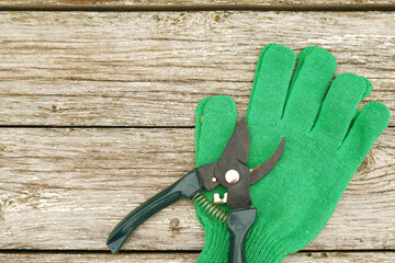 There are scissors with green pruning handles and green work gloves on a white wooden table. Garden hand pruners. Garden shears. Sharp trimmers for pruning trees and shrubs.Copyspace