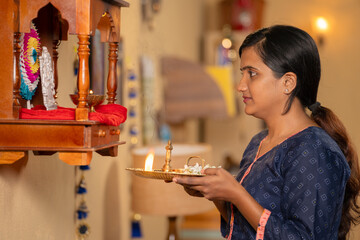 devotional young girl offering aarthi to god in front of mandapan at home at early morning -...