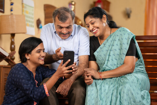 Indian teenager daughter showing Mobile phone app to middle aged parents at home - concept of social media sharing, Internet or technology and family bonding