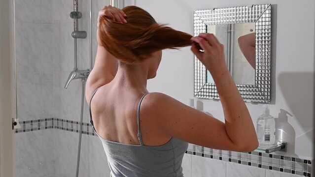 Woman from back, combing her hair in front of mirror in the bathroom. Long hair. 