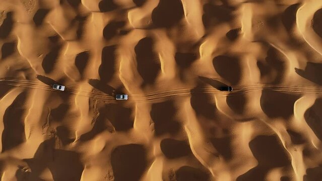 The drone is flying up looking topdown at three cars driving through the Sahara desert in Tunisia Aerial Footage 4K