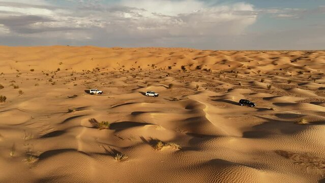 The drone is flying sideways following three cars driving through the Sahara desert in Tunisia Aerial Footage 4K