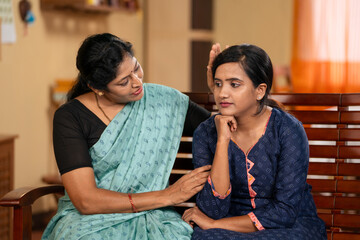 Indian middle aged mother consoling worried daughter at home - concept of parental care, family support and concern or compassion