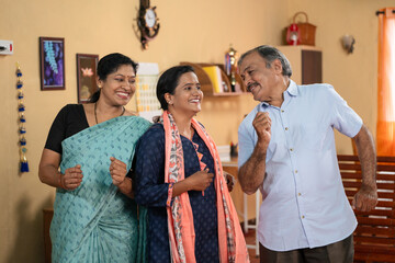 joyful Indian middle aged parents with teenager daughter dancing together at home - concept of good news, entertainment, harmony or family bonding.