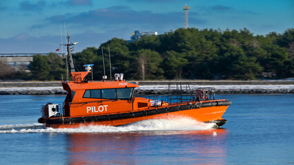 Fotografia pomarańczowej łódź pilota wpływającej kanałem portowym do Świnoujścia w efekcie panoramowania.