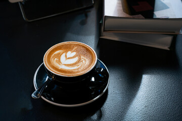 Hot coffee latte with latte art milk foam in cup mug on black wood desk on top view. As breakfast...