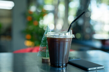 Americano iced coffee or black coffee in cup with smartphone and small Christmas tree on wood desk on top view In a coffee shop at the cafe,during business work