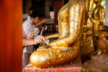 Close-up asian woman tourist Gilding gold leaf to Buddha for worship with faith to Buddha statue in temple thailand belief in Buddhism