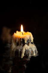 A burning candle in close-up, an antique candlestick covered with wax and cobwebs on a black background