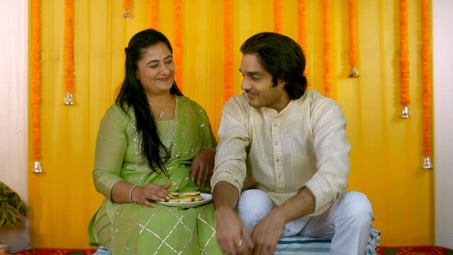 Loving Indian mother feeding her son Barfi - traditional sweet  ethnic family  Hindu wedding rituals. Handsome groom touching his aunts feet - showing respect  seeking blessing  Indian marriage cus...