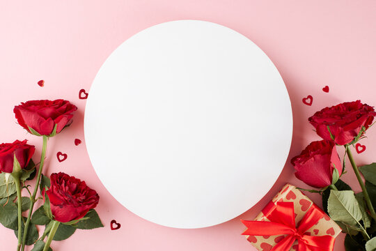 Selecting Valentine's day presents concept. Top view photo of red roses, gift box, festive sparkles on light pink background with blank circle for promo or message