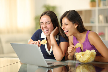 Two joyful friends watching media eating potato chips