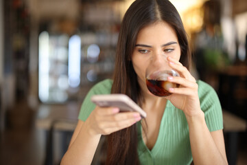 Woman in a bar checking phone and drinking