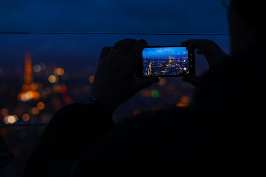 Travel to Paris. Close up selective focus photo with tourists taking photos and filming the beautiful evening panorama of Paris from above.