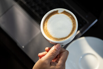 Business women hand holding white latte coffee cup and laptop on black table background.Hot coffee...