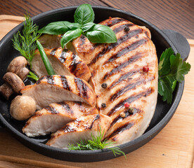 Roasted chicken fillet and mushrooms with herb in the frying pan on the wooden table close-up.