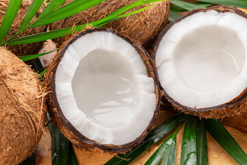 Fresh opened coconuts along with whole coconuts and coconut leaves on a wooden table.