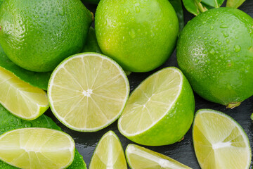 Ripe lime fruits with slices and lime leaves on a gray stone table.