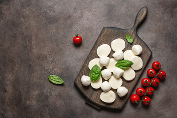 Mozzarella cheese balls and slices with basil leaves and cherry tomato on a dark background. Top view, flat lay, copy space.